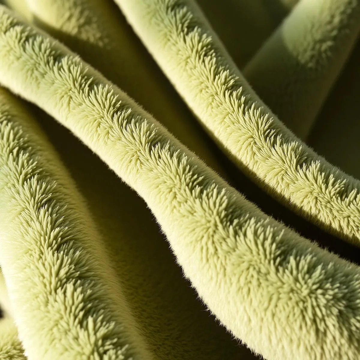 Close-up of soft, pale green plush fabric draped in folds, its fluffy pile lit by warm side light.