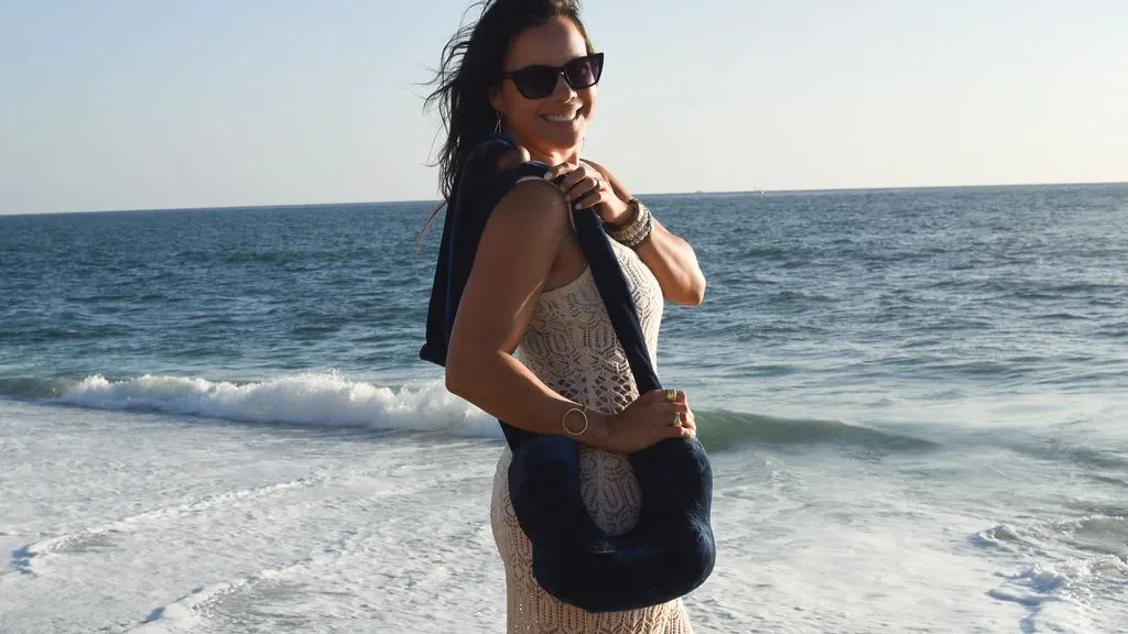 Founder standing near ocean sunset with Cruz pillow hanging on her arm like a purse